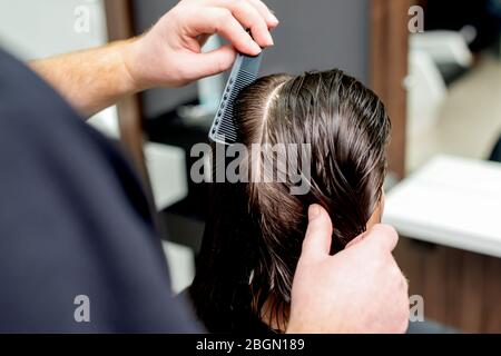 Le mani del parrucchiere stanno pettinando i capelli bagnati della donna nel salone dei capelli. Foto Stock