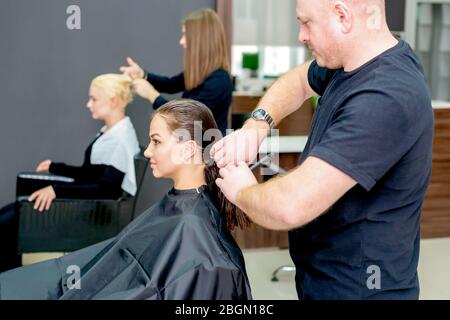 Due donne ricevono un taglio di capelli da due parrucchieri nel salone di parrucchiere. Foto Stock