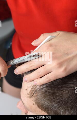 La moglie taglia i capelli sulla testa del marito a casa nel bagno Foto Stock