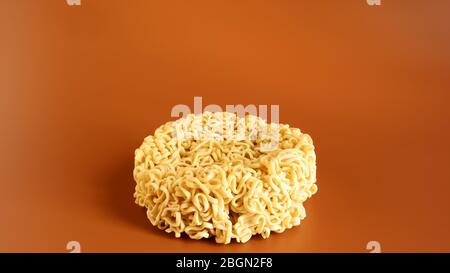 Pasta coreana istantanea a forma di cerchio su sfondo marrone. Vermicelli crudi, essiccati giallastro-bianchi, con lunghe linee rotonde e ritorti in dif Foto Stock