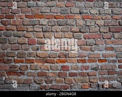 Frammento di un muro medievale del castello fatto di mattoni vari nella forma e colore, tonalità rosso scuro Foto Stock