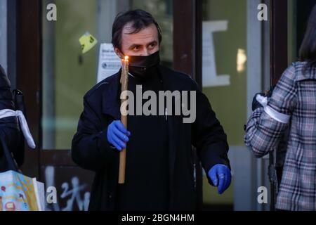 Bucarest, Romania - 18 aprile 2020: Un sacerdote ortodosso che indossa guanti e maschera a causa del blocco pandemico covid-19 consegna la luce Santa durante la t Foto Stock