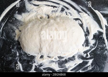 Primo piano di pasta bianca in polvere per la cottura del pane. Pasta bianca rotonda fatta a mano su un tavolo da cucina Foto Stock