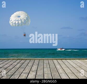 Piattaforma di legno vuota accanto alla spiaggia tropicale a Punta Cana, Repubblica Dominicana. Ala parasail bianca che vola sull'acqua del mare di Sargasso sullo sfondo Foto Stock