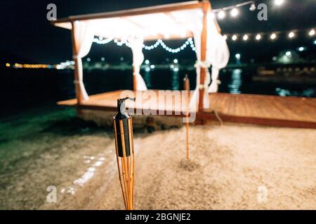 Torcia sul mare. Festa di notte in spiaggia. Una pergola con ghirlande Foto Stock