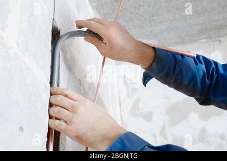 Worker man Installation of pipe channel for connecting air conditioner in concrete wall Foto Stock