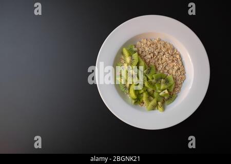 Avena fiocchi e fette di kiwi in un piatto bianco su sfondo scuro Foto Stock