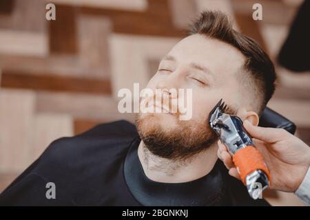 Il cliente hippster che visita nel barbiere rasa la barba Foto Stock