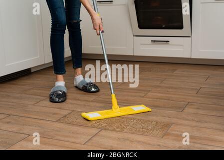 Vale la pena di pulire a casa una casalinga il pavimento. Bella donna lava pavimenti in legno da un laminato in una cucina luminosa. Foto Stock