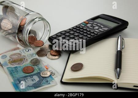 Bottiglia di vetro caduta, versando monete su un tavolo bianco con banconote, calcolatrice, notebook e penna Foto Stock