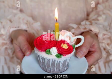 Torta di compleanno decorata con splendidi fiori a forma di panna montata con una candela brillante in mano alla donna Foto Stock