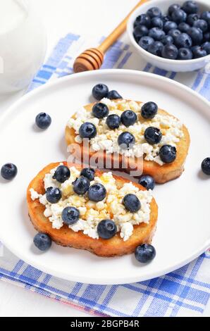 Panini con formaggio spalmabile, mirtilli e miele sulla piastra bianca Foto Stock