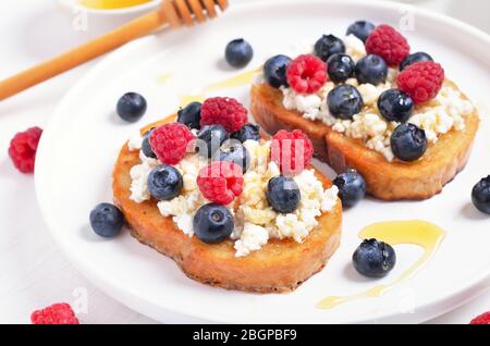 Panini con mirtilli, lamponi e miele su pane tostato con ricotta, vista ravvicinata Foto Stock