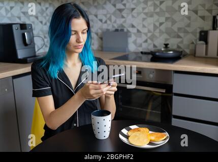 Bella giovane hipster donna scattando una foto della sua colazione in cucina moderna Foto Stock