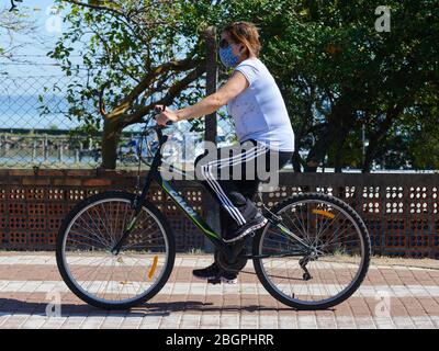 Donna in bicicletta utilizzando una maschera di protezione facciale a Coronavirus durante l'epidemia. Attività fisica pratica durante COVID-19 a Porto Alegre, Brasile. Foto Stock