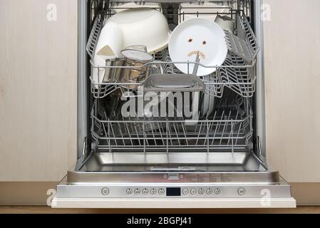 Piatti lavati male in lavastoviglie. Lavastoviglie integrata con piastre bianche davanti a vew e triste emozione su piastra. Macchina lavastoviglie rotta concetto Foto Stock