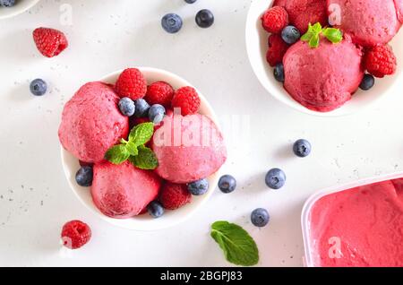 Gelato al lampone con lamponi freschi e mirtilli in ciotola su sfondo di pietra. Dessert estivo freddo. Vista dall'alto, disposizione piatta Foto Stock