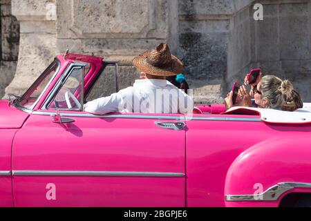 Donne turisti a l'Avana, Cuba, con un giro in una classica Chevrolet rosa con un autista locale cubano. Donne che fotografano con lo smartphone. Foto Stock