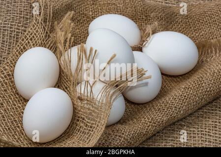 Uova di pollo bianche avvolte in burlap accanto ad un cesto su un bianco uova su sfondo burlap Foto Stock