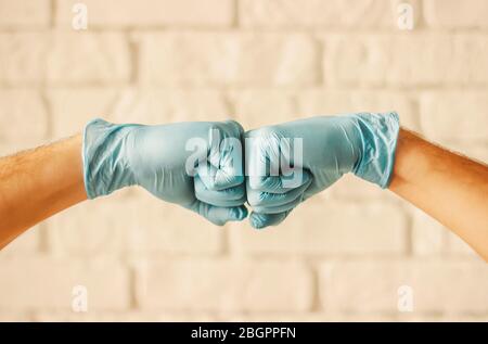 Due uomini che urtano le mani con guanti medici blu come protezione contro il coronavirus. Medici chirurghi in guanti di lattice protettivo blu che si aggrafano i pugni. COVID- Foto Stock