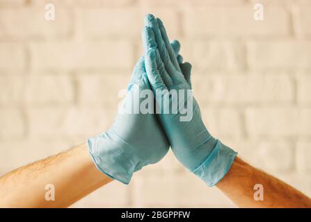 Due uomini che si aggrabilano le mani nei guanti protettivi. Medici che indossano guanti medici sulle mani per celebrare il successo in ospedale. Nuovo saluto Palm. COVID-19 Prev Foto Stock