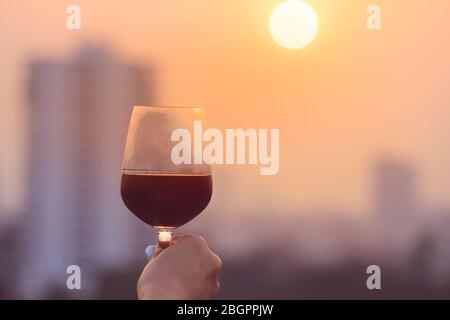 Mano della donna che tiene i bicchieri di vino rosso sul balcone durante il tramonto, concetto di festa Foto Stock