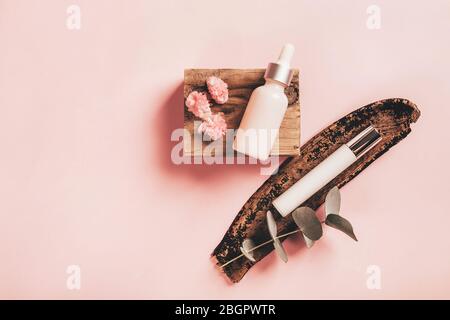 Bottiglie cosmetiche su barre di legno con fiori di eucalipto e begonia su sfondo di carta rosa. Concetto di salute e bellezza. Foto Stock