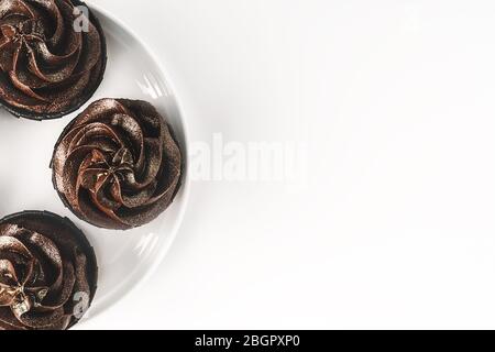 Deliziosi cupcake al cioccolato con glassa al cioccolato e spruzzati d'oro su piastra in porcellana bianca su sfondo bianco isolato. Mockup per il tuo d Foto Stock