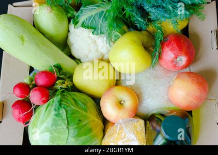 Scatola con frutta e verdura mele cavolo rafano olio zucchine, grits primo piano. Servizi di consegna di cibo durante la pandemia di coronavirus e sociale Foto Stock