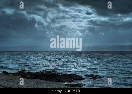 Raggi del sole che si infranono attraverso nuvole scure sulla riva del mare sulla costa settentrionale dell'isola di Arran, Scozia Foto Stock