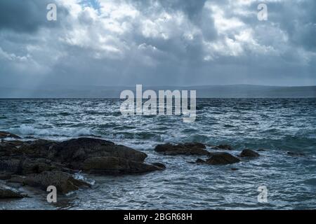 Raggi del sole che si infranono attraverso nuvole scure sulla riva del mare sulla costa settentrionale dell'isola di Arran, Scozia Foto Stock