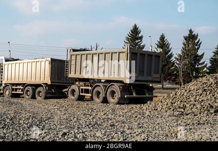 Un dumper scarica la ghiaia in un cantiere. Il dumper scarica il suo carico di ghiaia in un nuovo progetto di costruzione stradale. Edificio stradale Foto Stock