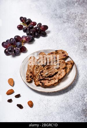 Pane di frutta a fette su un piatto con uve rosse, colofonia e mandorle. Concetto di cibo sano fatto in casa. Messa a fuoco selettiva. Spazio di copia. Foto Stock