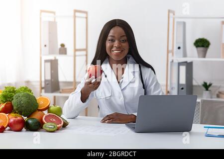 Un medico nero sorridente che consiglia di mangiare frutta fresca Foto Stock