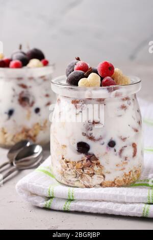 Muesli di miele croccante alla granola con ribes nero e rosso surgelato e yogurt naturale, una deliziosa e salutare colazione, situata in vasetti di vetro su un grigio Foto Stock