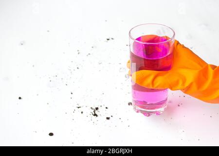 Liquido rosa in una tazza di vetro, la mano in un guanto protettivo tiene un bicchiere Foto Stock