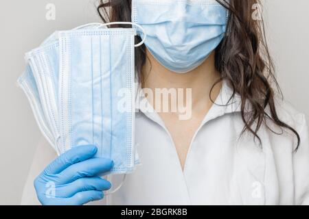 Arrestare SARSCoV, virus 2020, COVID-19. Le mani di Womans nei guanti medici blu che tengono una maschera protettiva. Medico che indossa la maschera facciale di protezione contro Foto Stock