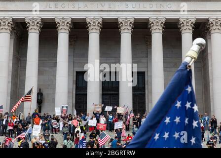 Le bandiere americane sono viste di fronte a persone che hanno segni di protesta contro le restrizioni di soggiorno a casa durante la pandemia COVID-19 sui passi di t Foto Stock