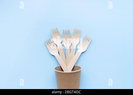 utensili da cucina monouso ecologici su sfondo blu. forchette e cucchiai in legno in tazza di carta. ecologia, concetto zero rifiuti. vista dall'alto. disposizione piatta Foto Stock