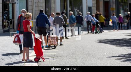 Chartres, Francia - Avril 18, 2020: Persone in attesa in linea rispettando la distanza sociale rulles per accedere a un mercato di strada aperto, durante la chiusura t Foto Stock