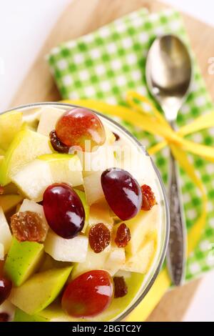 Colazione sana - yogurt con fette di uva fresca e mele e muesli serviti in una ciotola di vetro su un vassoio di legno, primo piano Foto Stock