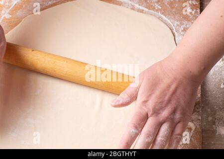 Mani femminili che rotolano l'impasto su un tagliere con un perno di laminazione. Cucina a casa. Foto Stock