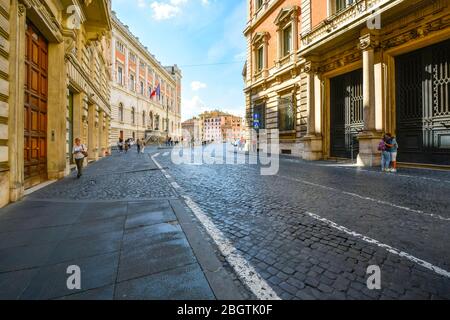 Un paio di abbracci sul marciapiede mentre i turisti e la gente del posto camminano lungo un'ampia strada vuota vicino a Piazza Navona a Roma Foto Stock