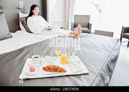 Donna d'affari che fa colazione a letto in un hotel di lusso Foto Stock
