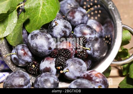 Prugne dolci mature in colapasta metallica, su tavola di legno Foto Stock