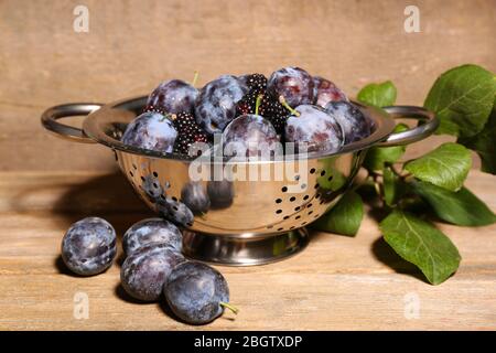 Prugne dolci mature in colapasta metallica, su tavola di legno Foto Stock