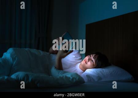 Donna asiatica che si avvale di un tablet digitale che naviga su Internet per guardare film o videochiamare con un amico sul letto Foto Stock