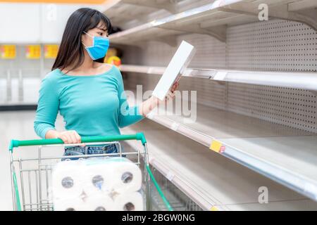 Donna asiatica che guarda Supermarket vuoto cornflakes box scaffali in mezzo COVID-19 paure coronavirus, acquirenti panico di acquisto e stoccaggio di cibo preparazione Foto Stock
