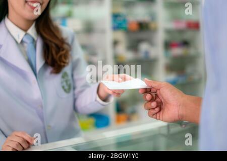Fiducioso asiatici femmina giovane farmacista con un bel sorriso amichevole e di ricevere il farmaco prescrizione da uomo paziente in farmacia farmacia. Med Foto Stock