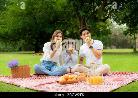 Asian teen famiglia felice momento pic-nic vacanza nel parco con padre, madre e figlia mangiare mela verde e sorridere per trascorrere felice tempo di vacanza t Foto Stock